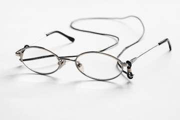 Close-up of old shabby scratched oval metal eyeglasses featuring a black neck strap, placed on a clean white surface for product or accessory visuals.