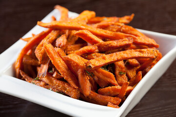 A pile of sweet potato fries on a white plate on a dark background. 