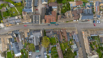 Aerial view of a quaint town bisected by a straight road, where cars traverse between buildings with varied rooftops, creating a tapestry of textures and tones, Corsham, Wiltshire, United Kingdom.