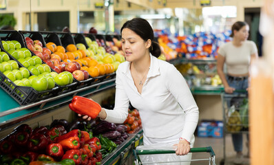Young woman shopper in casual clothes buys bell pepper at grocery store..