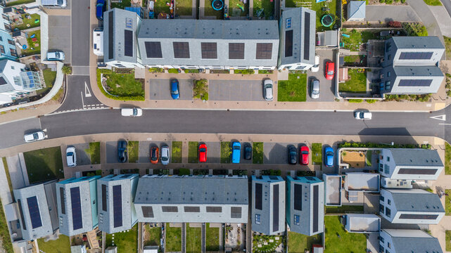 Aerial view of neat rows of houses with solar panels, interspersed with colorful cars and green lawns, capturing the essence of modern suburban living, Saint Austell, United Kingdom.