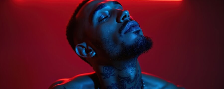 Close up photo of person. Male model with eyes closed against red and blue neon light. Artistic portrait highlights skin texture. Intense expression of peace.