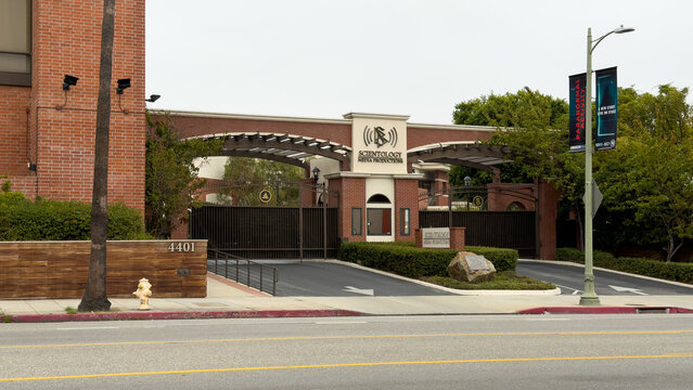 Street view of Scientology Media Productions in Hollywood, showing gated entrance, brick construction, security features, and surrounding urban environment with signage