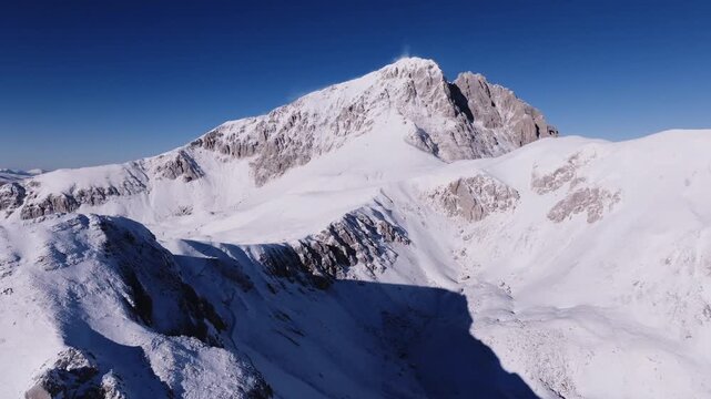 Majestic Snow-Capped Mountain Range Under Brilliant Blue Sky: Rugged Winter Landscape with Dramatic Shadows and Serene Vistas, Perfect for Nature and Travel Themes.