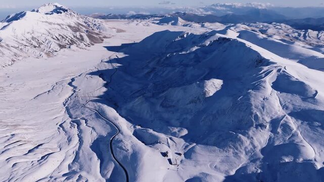 Stunning aerial drone footage over the snow-covered Gran Sasso mountain range in Italy. A cinematic flight above a winding road in the vast, majestic winter landscape. Cinematic 4K