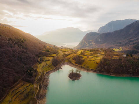 Aerial view of the intensely turquoise lake mirroring the surrounding rugged mountains and terraced hillsides under a soft, diffused light, Tenno, Trentino-South Tyrol, Italy.