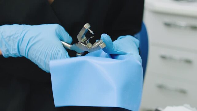 Dental professional prepares tools for a procedure in a clinic setting with blue sterilization drapes in a bright environment