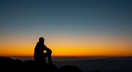 Silhouette of a person contemplating a mountain vista at sunset