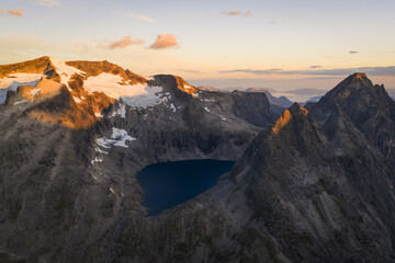 Aerial view of a glacial lake nestled amidst rugged, snow-capped peaks catching the warm glow of the setting sun, Trollstigen, More og Romsdal, Norway.