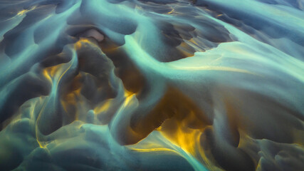 Aerial view of glacial rivers intertwining, creating a mesmerizing display of turquoise and gold hues on the rugged terrain, Hvolsvollur, Rangarbing eystra, Iceland.