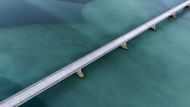 Aerial view of a long bridge cuts a stark line through the turquoise water, contrasting the man-made structure against the natural expanse, Hvolsvollur, Rangarbing eystra, Iceland.