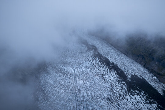Aerial view of an icy river winding through the landscape, shrouded in mist and cloud, Skaftafell, Sveitarfelagid Hornafjordur, Iceland.
