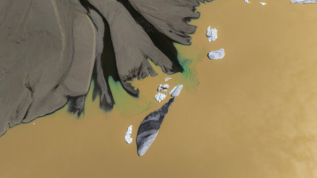 Aerial view of glacial rivers carve through ochre sands, scattered with ice floes and algae bloom, creating a surreal landscape, Skaftafell, Sveitarfelagid Hornafjordur, Iceland.