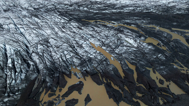 Aerial view of glacial ice contrasting sharply with dark volcanic ash and meltwater streams, creating a stark landscape, Skaftafell, Sveitarfelagid Hornafjordur, Iceland.