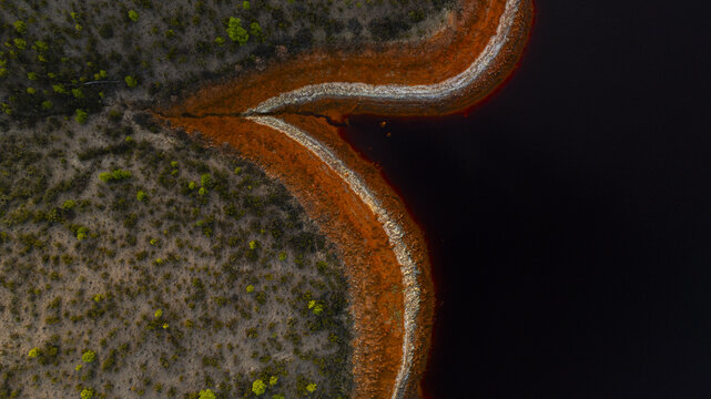 Aerial view of the stark contrast between the reddish-brown earth and the dark, still waters of R&iacute;otinto, creating a surreal landscape of textures and tones, R&iacute;otinto, Andalusia, Spain.