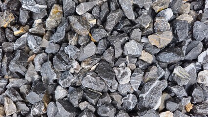 A hand holding a black and white stone, which is a natural mineral. The stone has a rough surface and white quartz-like crystals interspersed with black parts of other minerals.