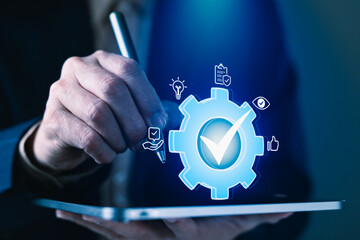 Businessman using stylus on tablet with digital gear and check mark icon for quality assurance,...