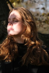 Fototapeta premium Face portrait of a young woman in sunny autumn park. Light and shadow