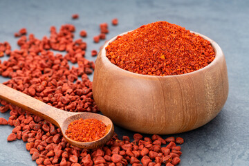 Ground or crushed organic annatto in the spoon and in the bowl - Bixa orellana