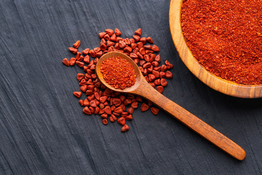 Ground or crushed organic annatto in the spoon and in the bowl - Bixa orellana