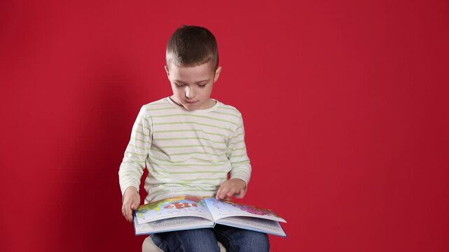 Cute little boy reading book on red background