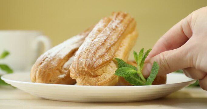 Woman adding mint to eclairs at white wooden table, closeup