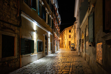 Illuminated buildings at night on an empty narrow cobblestone street in the medieval center of Rovinj, Croatia.