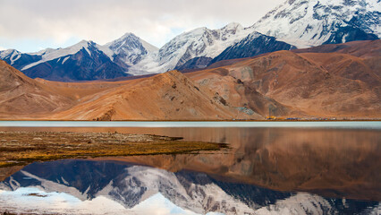 Scenic reflection of snow-capped Muztagh Ata peak in Karakul Lake on the Pamir Plateau in Xinjiang...
