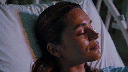 A serene close-up of a woman resting in a hospital bed, captured from a side angle. The video conveys calmness and recovery in a clinical setting.
