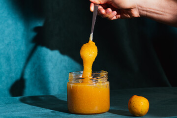 Hand scooping homemade quince jam from glass jar