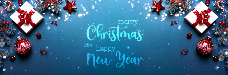 Merry Christmas and Happy New Year text on blue background with gift boxes, ribbons, red decoration, fir branches, bokeh, sparkles. Xmas and winter holidays. Christmas banner, top view