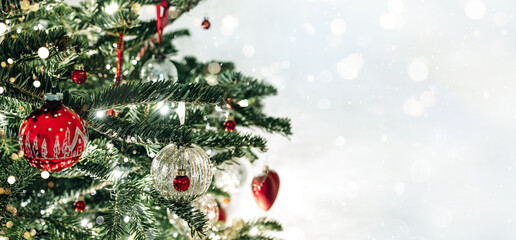 Christmas tree with red Christmas decorations on light background with bokeh, blurred, sparking, glowing. Happy New Year and Xmas card, wide banner