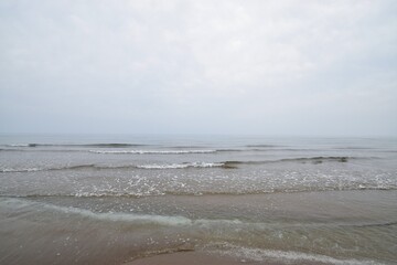 Calm waves gently washing onto a sandy beach under an overcast sky, depicting a quiet and melancholic winter seascape along the Sea of Japan.