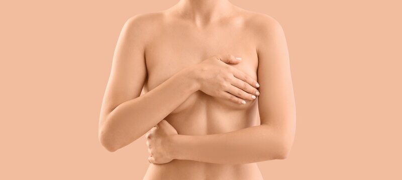 Naked young woman covering her breast on beige background, closeup