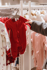 A girl looks at a red baby sleepsuit in a store.