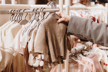 An unrecognizable girl examines a knitted baby cardigan on a hanger in a store.