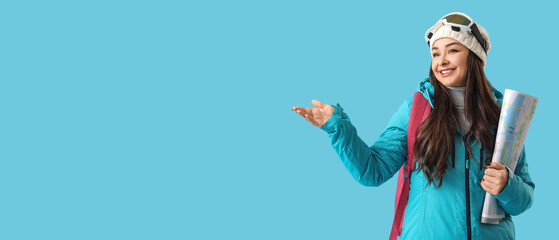 Female tourist in winter clothes and with map showing something on blue background with space for...