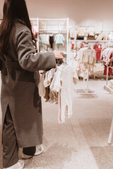 A brunette girl carries various baby clothes on a hanger in a store.