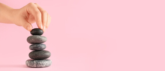 Hand putting pebbles in stack on pink background. Zen concept
