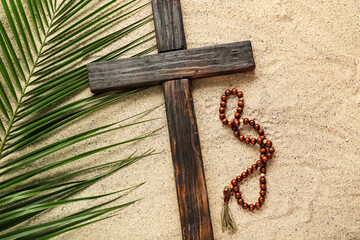 Wooden cross with prayer beads and palm leaf on sand. Good Friday concept