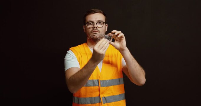 A worker in a safety vest puts on protective goggles over his regular eyeglasses, demonstrating proper workplace safety procedure.