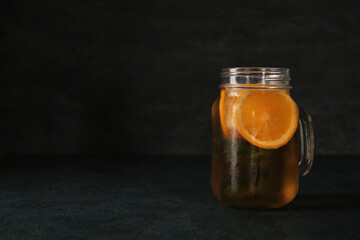 Mason jar of ice tea with orange on black background