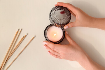 Woman holding burning candle with matches on beige background