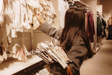 A girl chooses clothes for a newborn baby in the baby department.