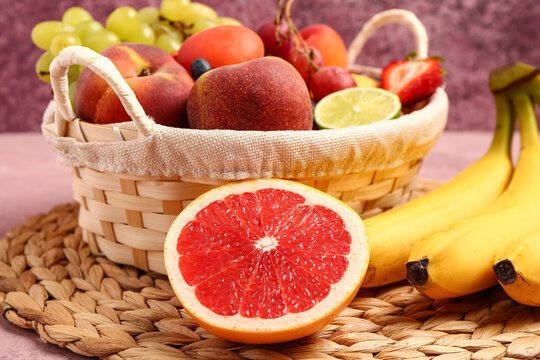 Wicker basket with different fresh fruits on pink table, closeup
