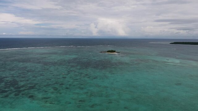 Aerial view of tiny island in the middle of the wide ocean with visible coral reef. Guyam Island. Siargao, Philippines.