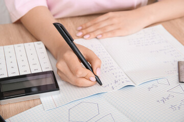 Naklejka premium Woman writing math formulas in copybook on wooden table