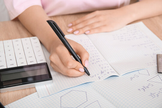 Woman writing math formulas in copybook on wooden table