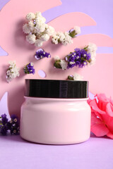 Composition with jar of cosmetic product and beautiful flowers on color background, closeup