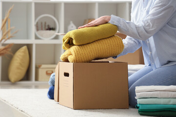 Young woman packing stack of clothes into cardboard box in bedroom, closeup